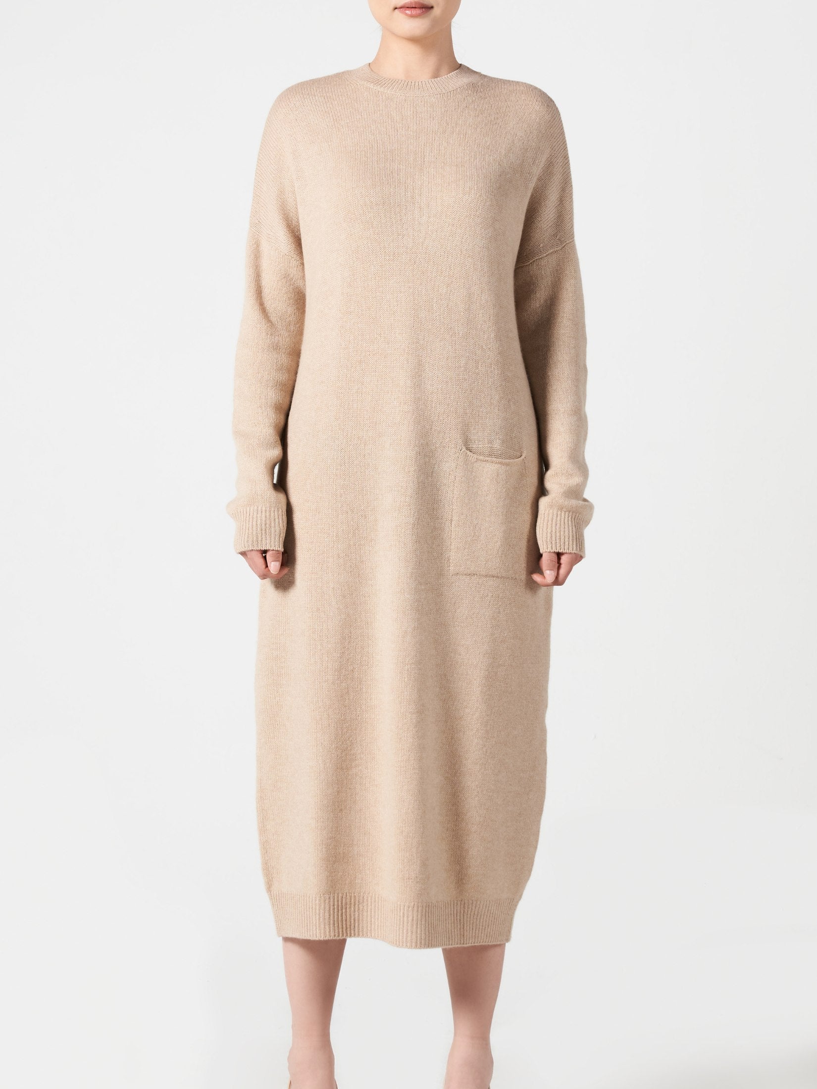 Woman wearing a relaxed fit beige cashmere dress with one pocket and long sleeves, minimalist design.
