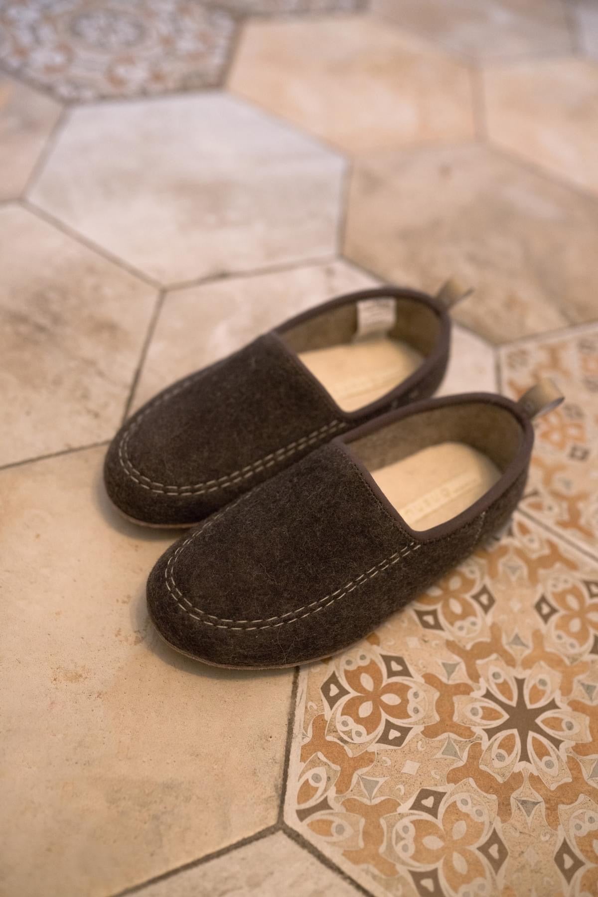 Brown felt slip-on slippers worn, highlighting their soft material and comfortable, casual design.