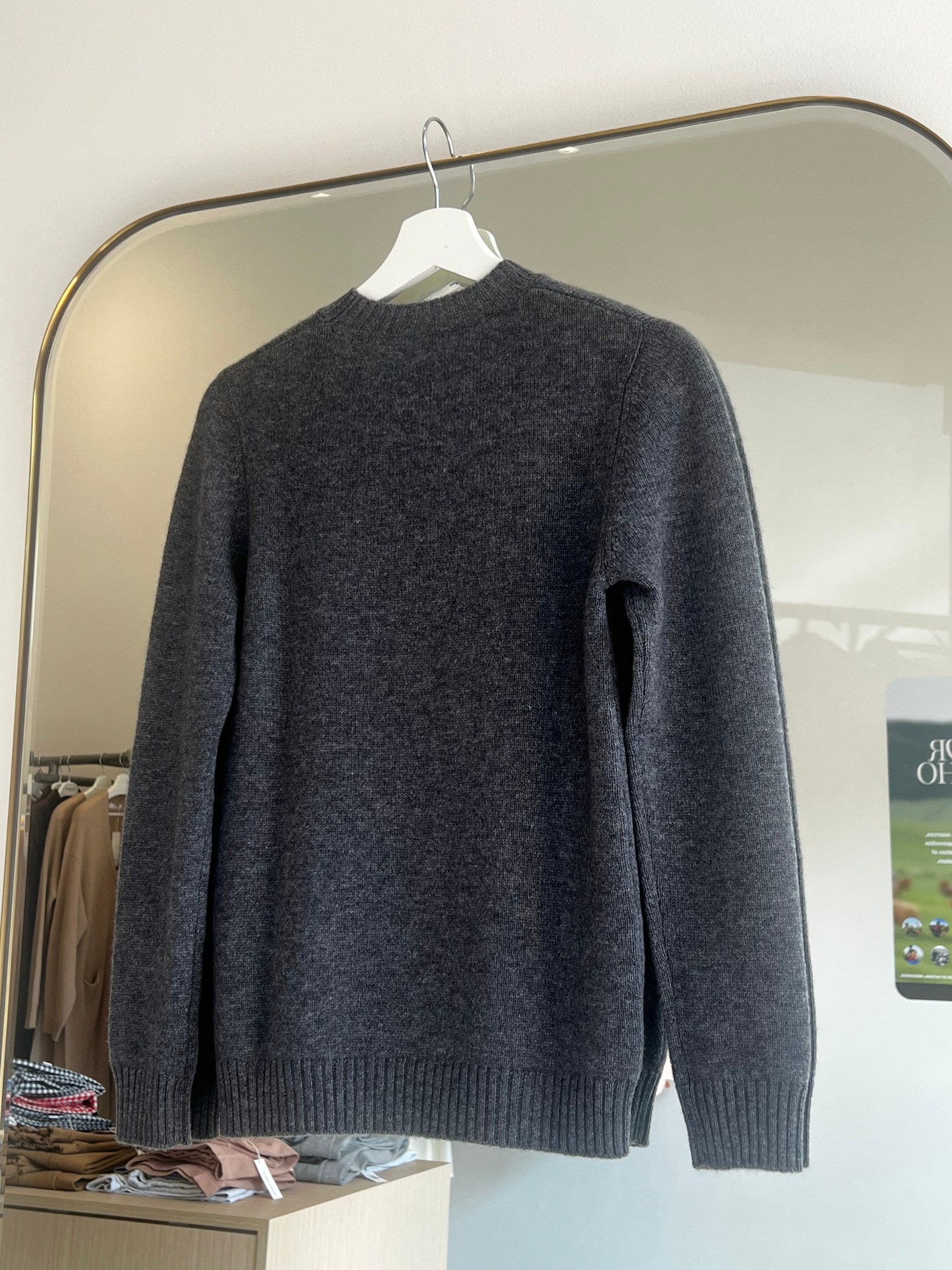 Dark gray round neck cashmere sweater hanging on white hanger against mirror background