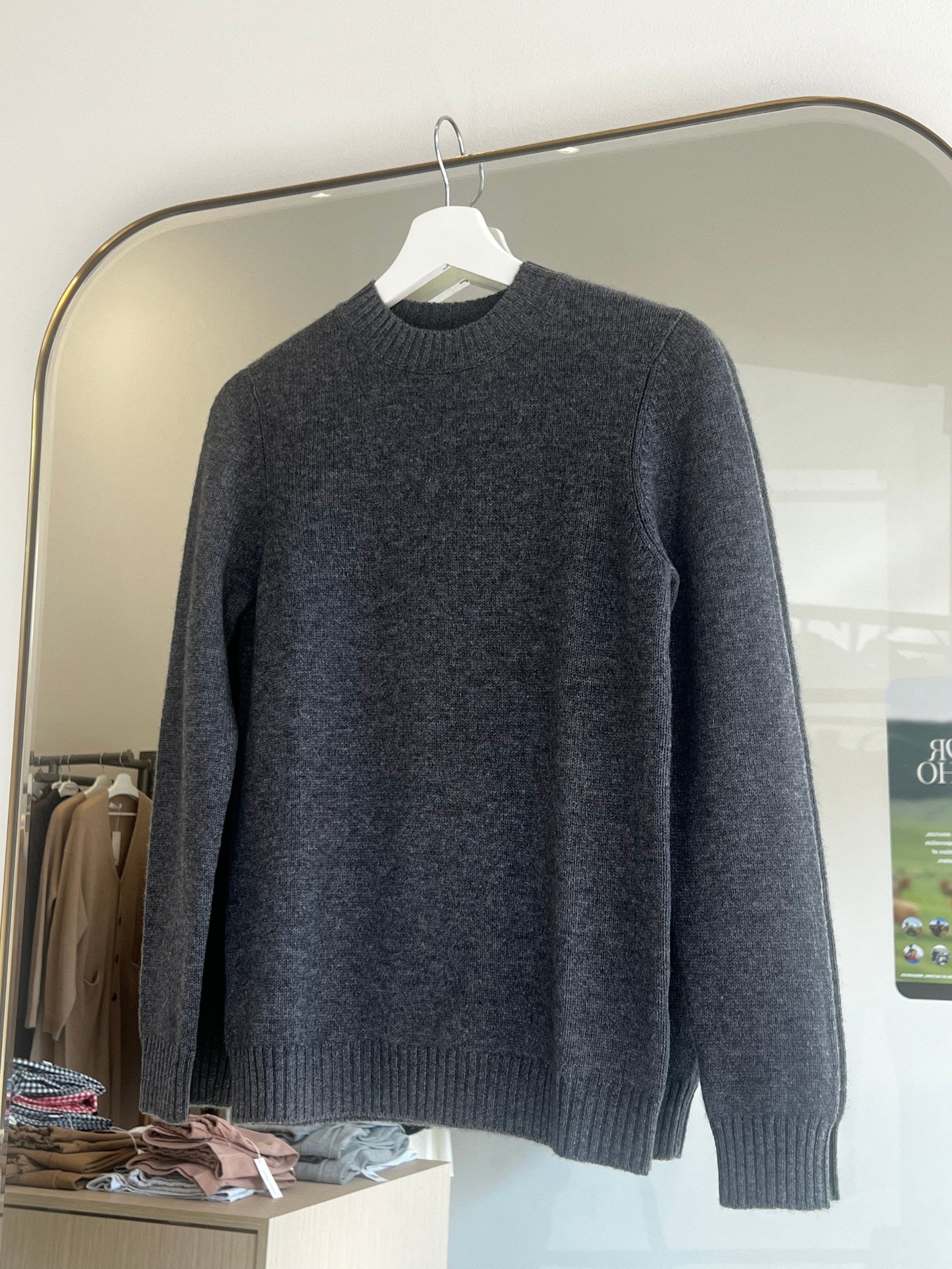 Dark grey round neck cashmere sweater hanging on white hanger in bright modern room interior