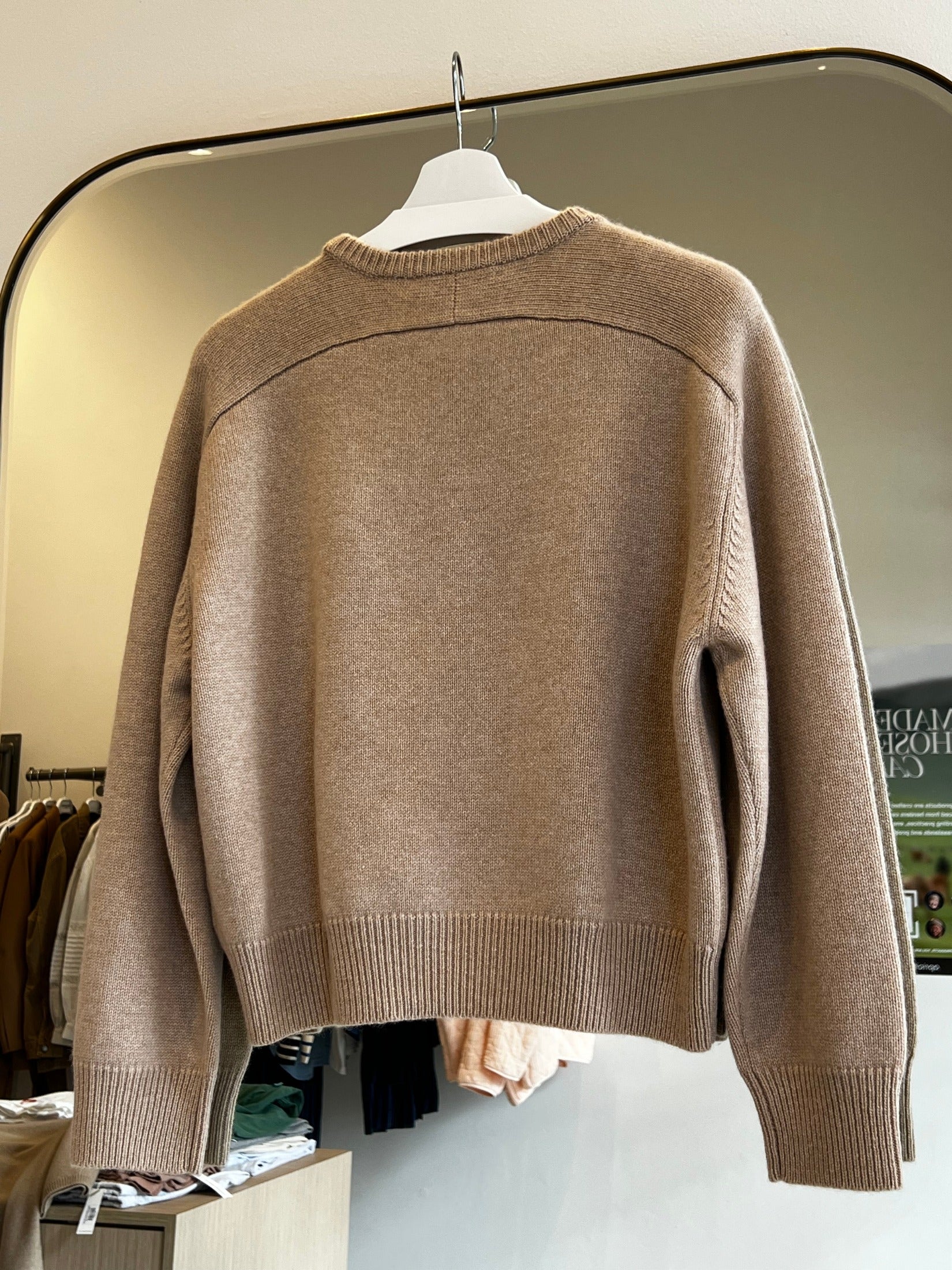 Beige round neck cropped cashmere sweater with raglan sleeves hanging on a white hanger in a store.