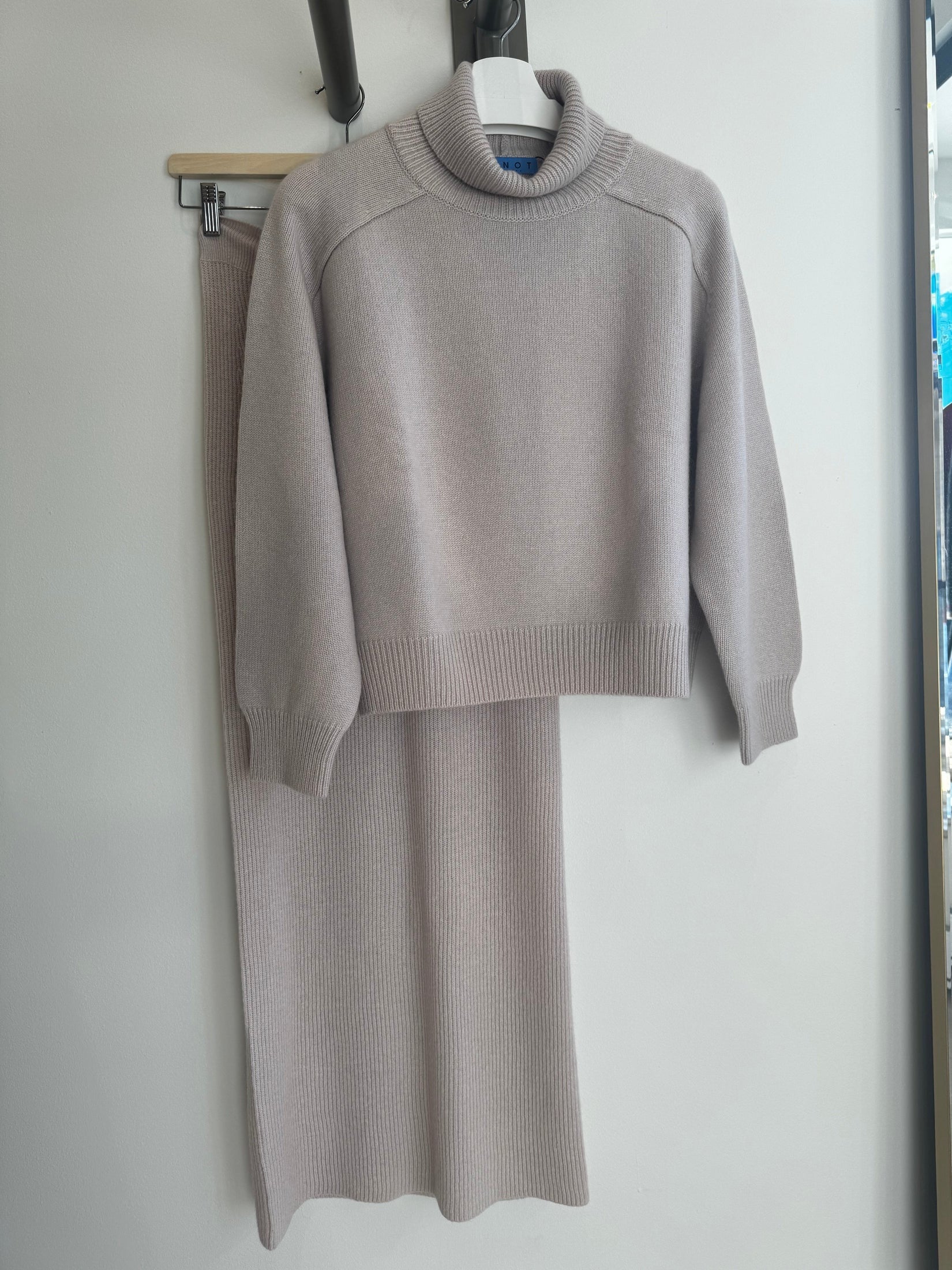 Cashmere turtleneck sweater on hanger, paired with a maxi cashmere skirt, showcasing a cozy, elegant design and soft, luxurious texture.