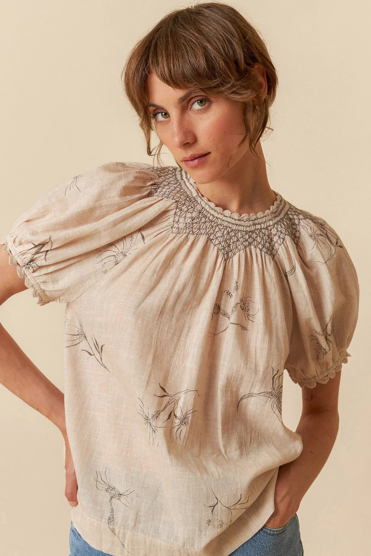 Model wearing a beige organic cotton short-sleeve blouse with flower and feather print.