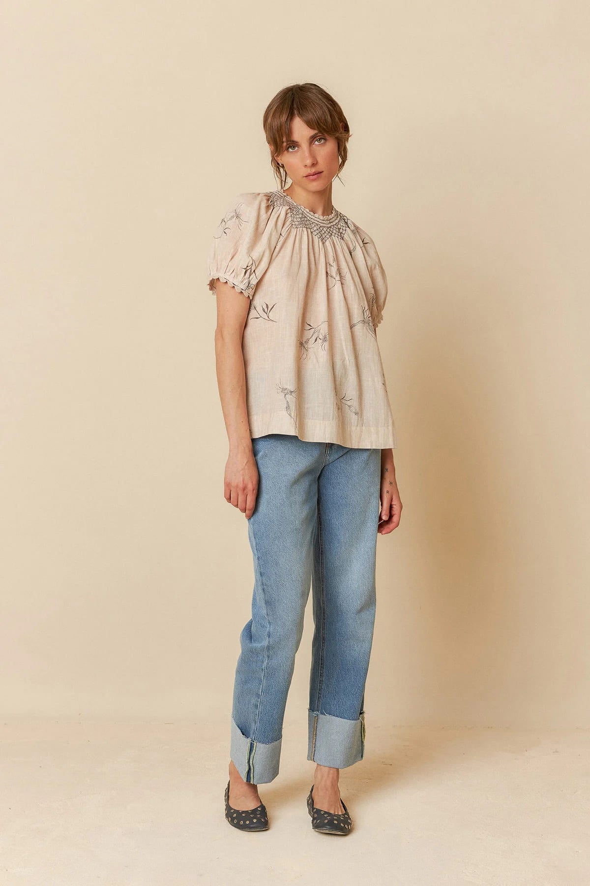 Model wearing a beige organic cotton short-sleeve blouse with flower and feather print.