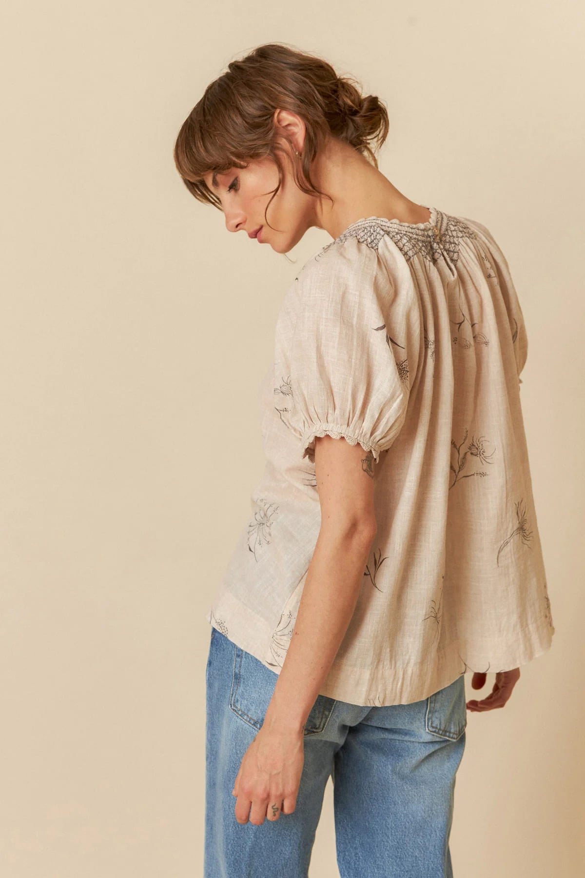 Model wearing a beige organic cotton short-sleeve blouse with flower and feather print.