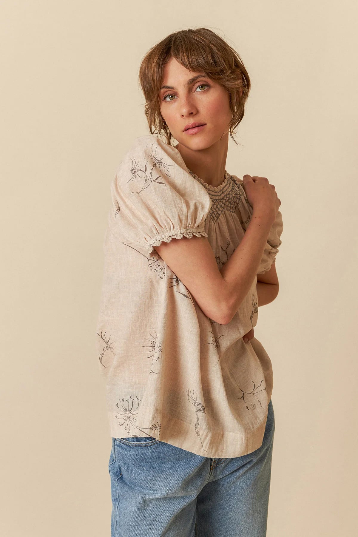 Model wearing a beige organic cotton short-sleeve blouse with flower and feather print.