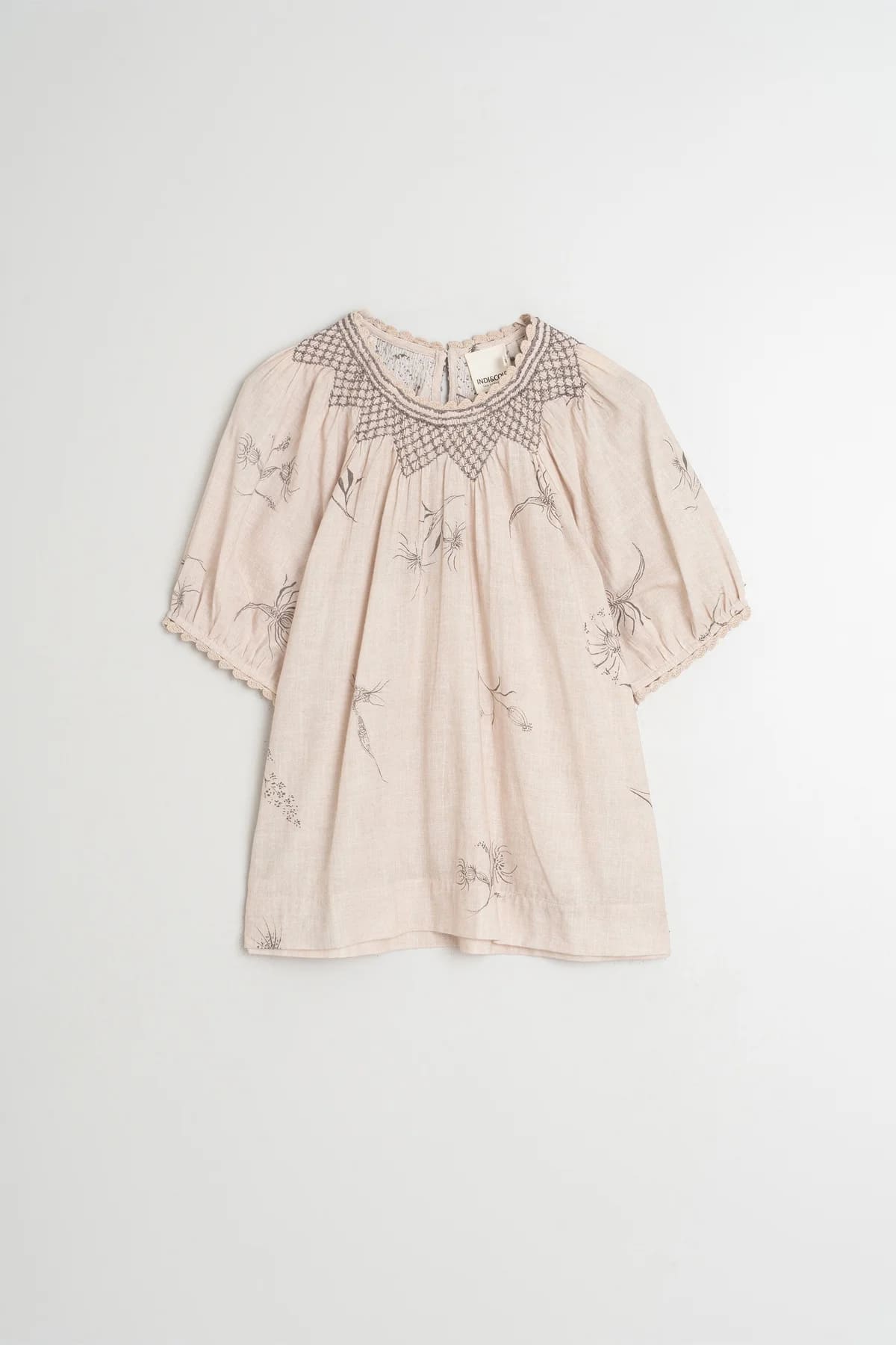 Flat lay of a beige organic cotton short-sleeve blouse with flower and feather print.