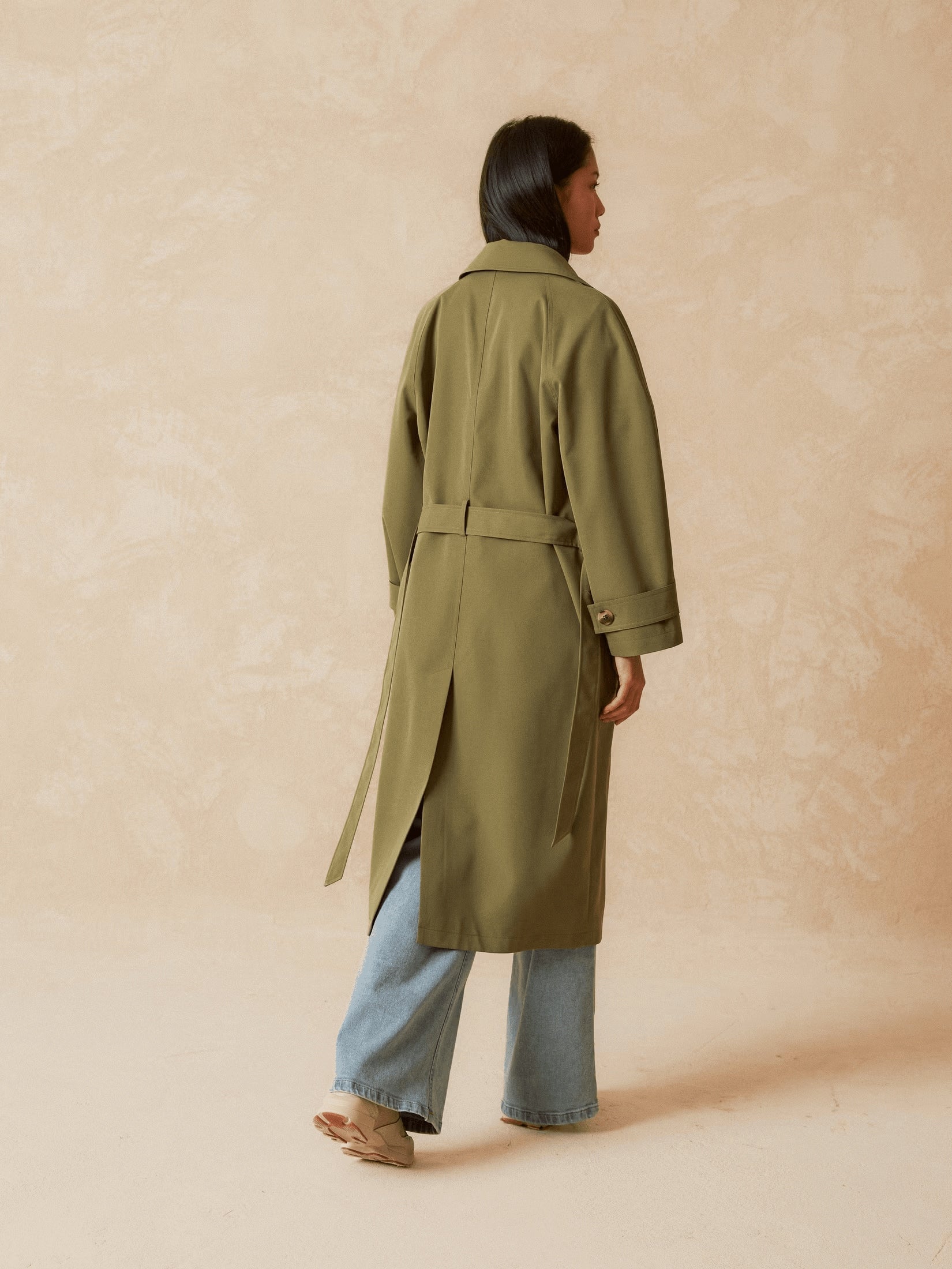 Back view of a model wearing a long khaki trench coat.