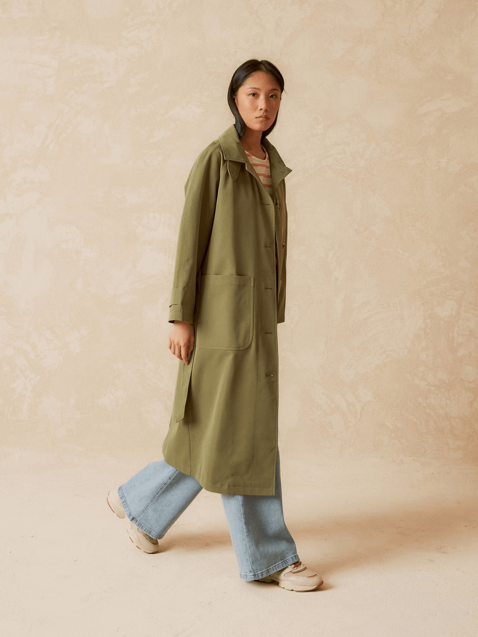 Front view of a model wearing a long khaki trench coat.