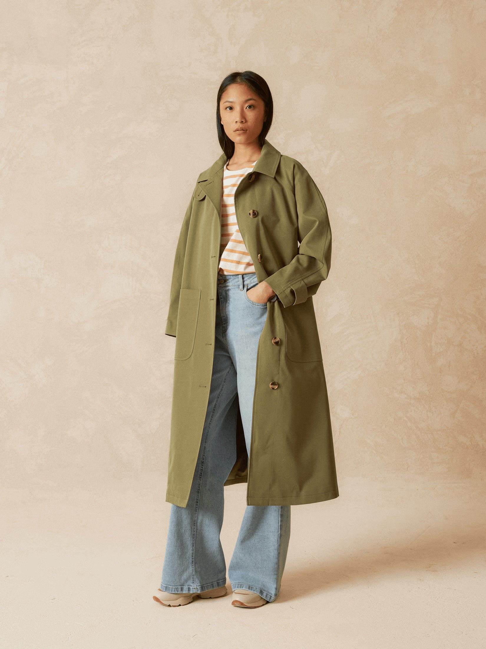 Front view of a model wearing a long khaki trench coat.