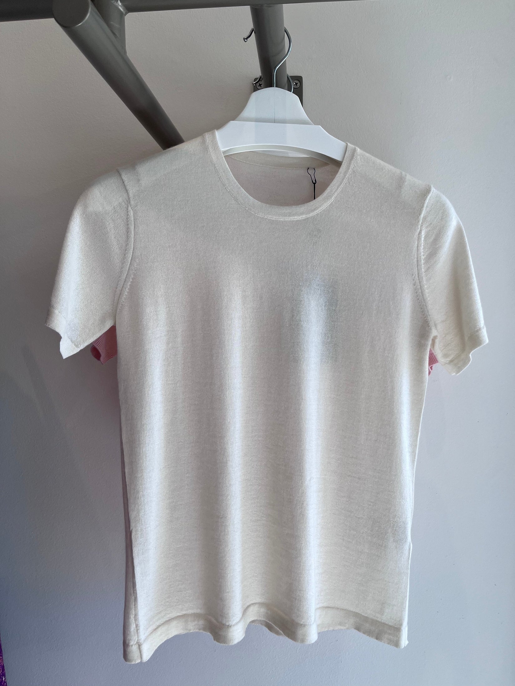 White silk-cashmere t-shirt on hanger, featuring a smooth, luxurious texture and classic, relaxed fit.